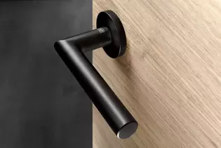 The picture shows the door handle Lucia in graphite black finish mounted on a wooden door.